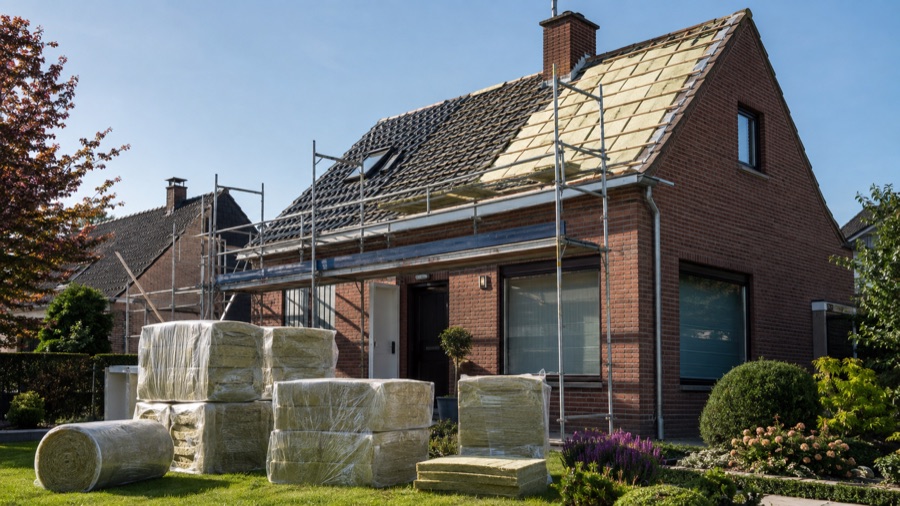 Vlaamse eengezinswoning waar dakisolatiewerken bezig zijn, met steiger tegen de gevel en isolatiemateriaal in de tuin